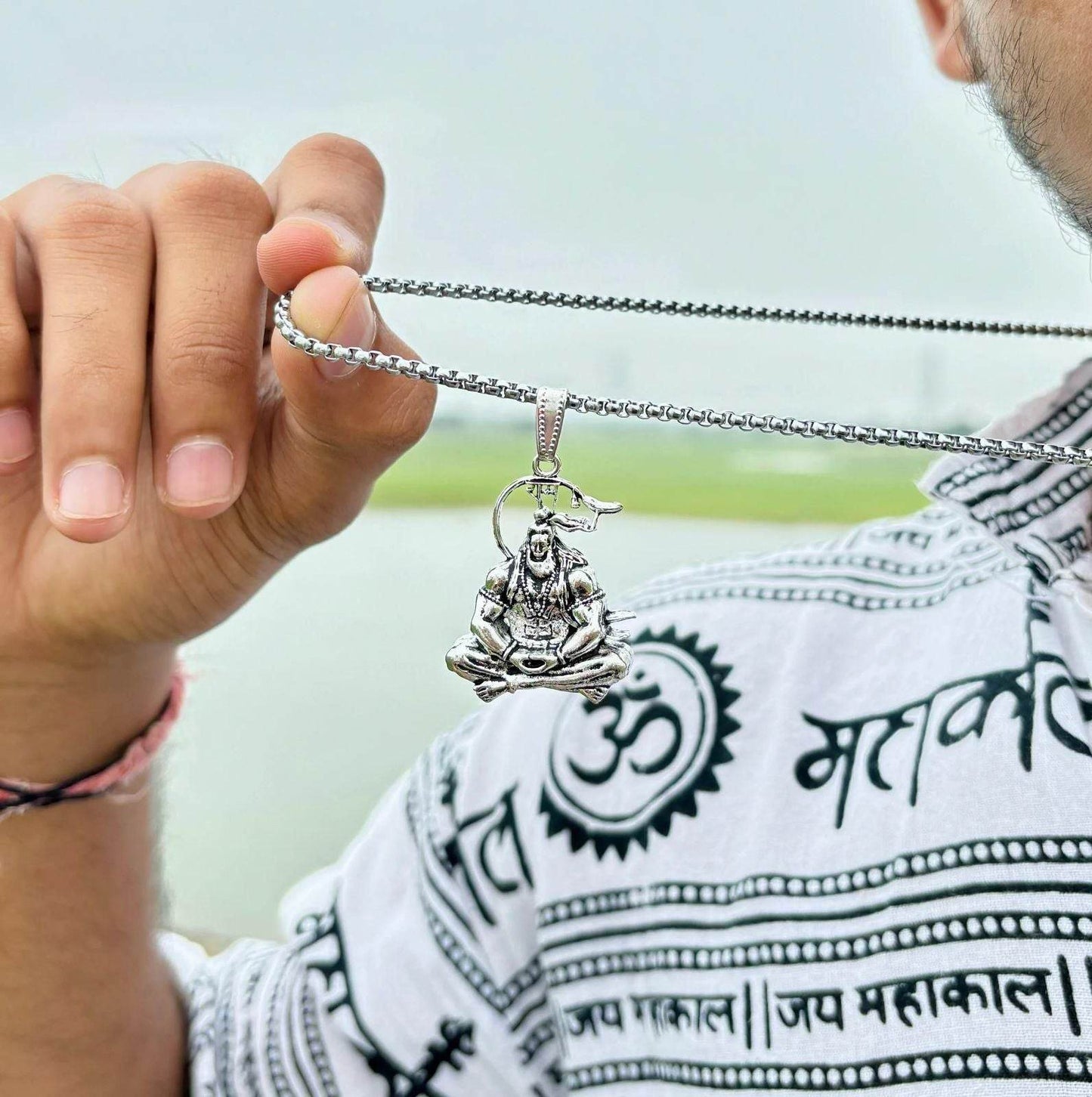 Hand holding silver Lord Hanuman pendant necklace with detailed figure on chain