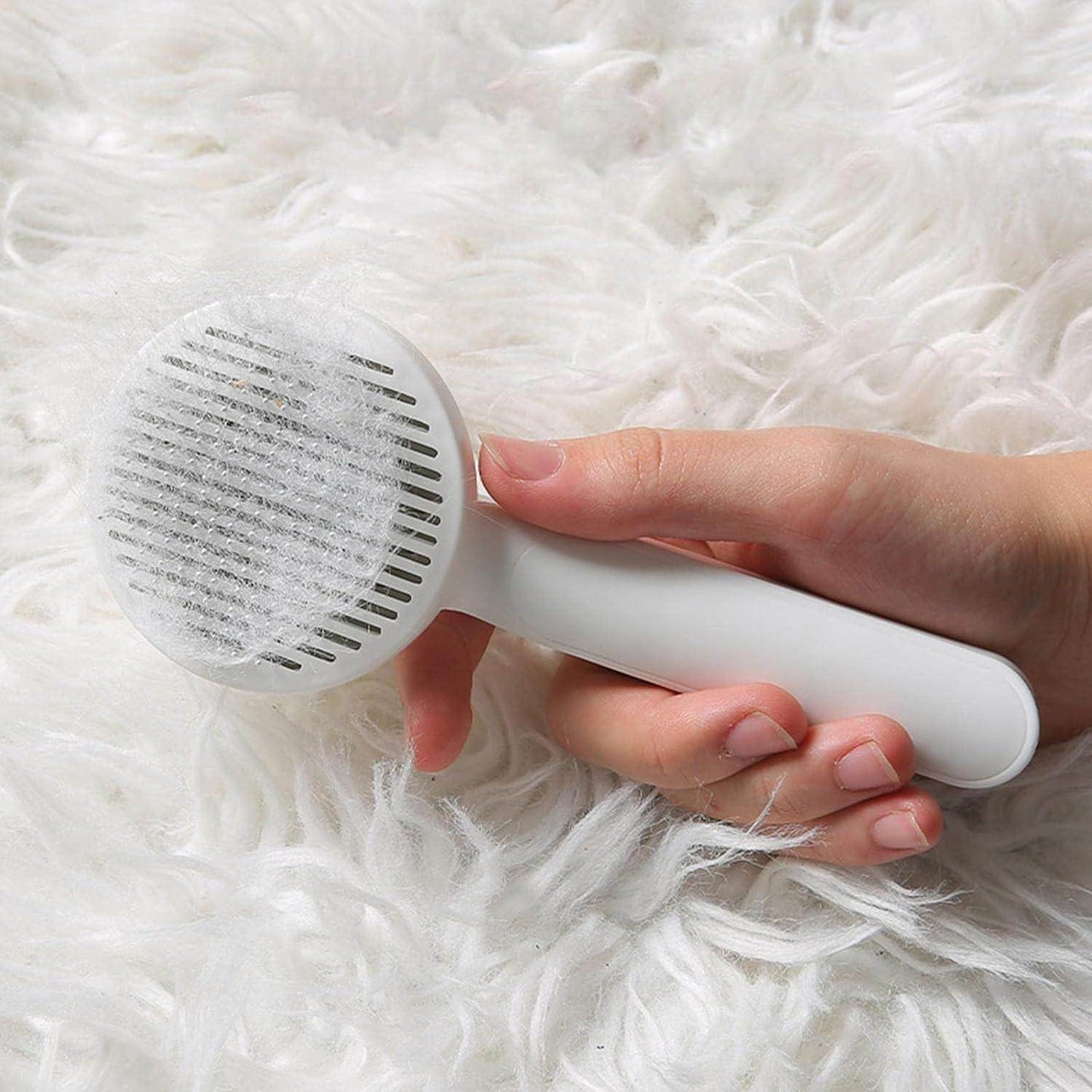 Hand holding a white pet head comb with cleaning needle filled with pet hair on a fluffy white surface