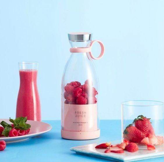 Portable mini juice blender with fresh strawberries inside and a freshly blended pink smoothie nearby