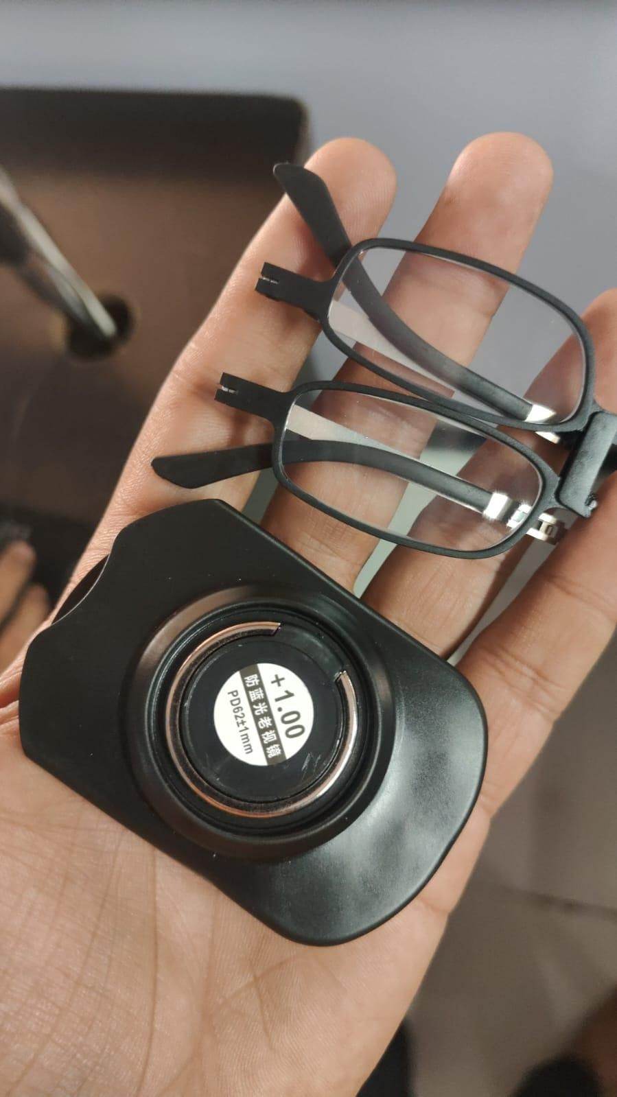 Black compact portable reading glasses UV400 with foldable frame and plus 1.00 magnification held in hand