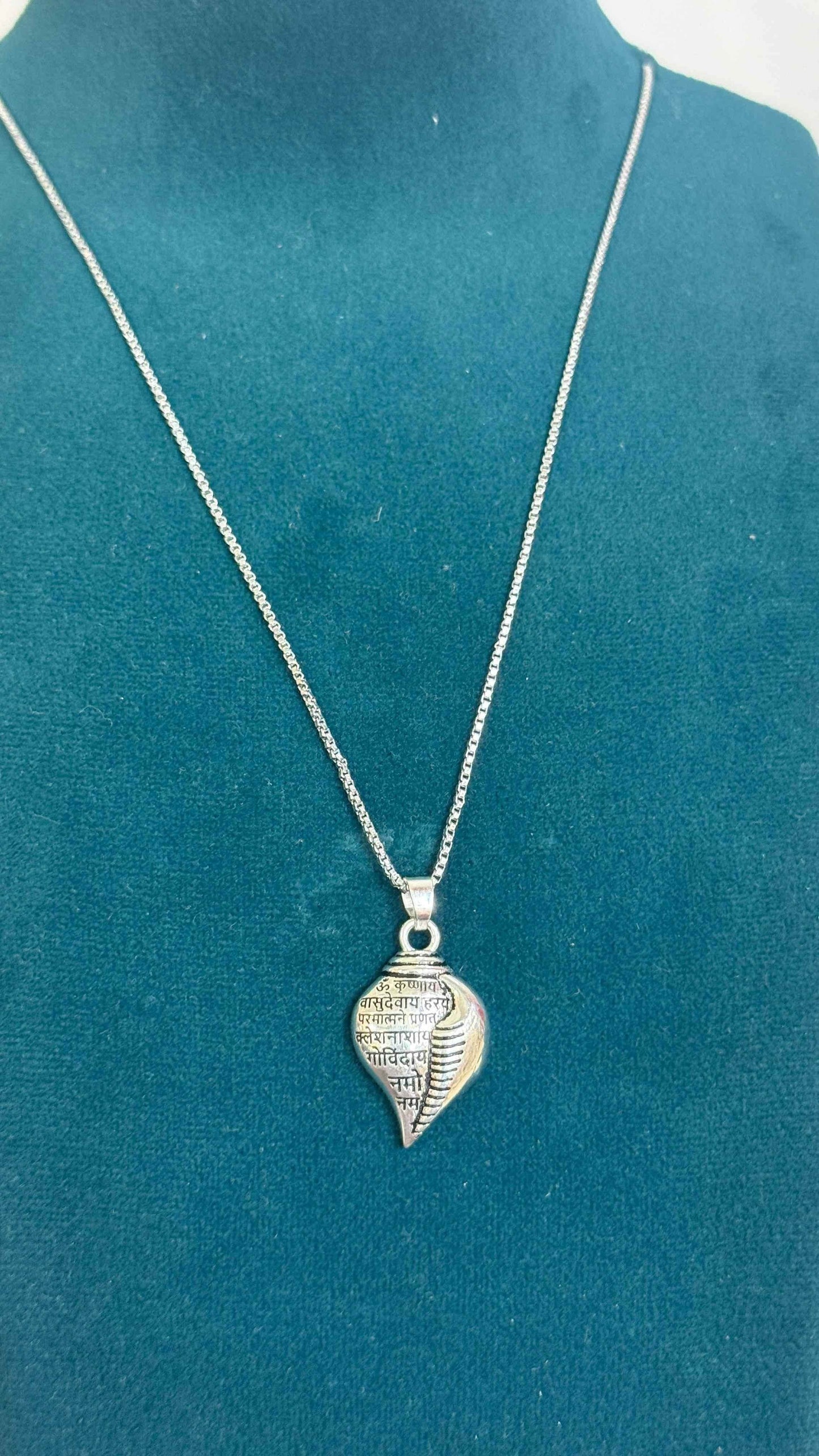 Silver Shri Krishna conch pendant necklace with intricate design on a chain displayed on a teal mannequin