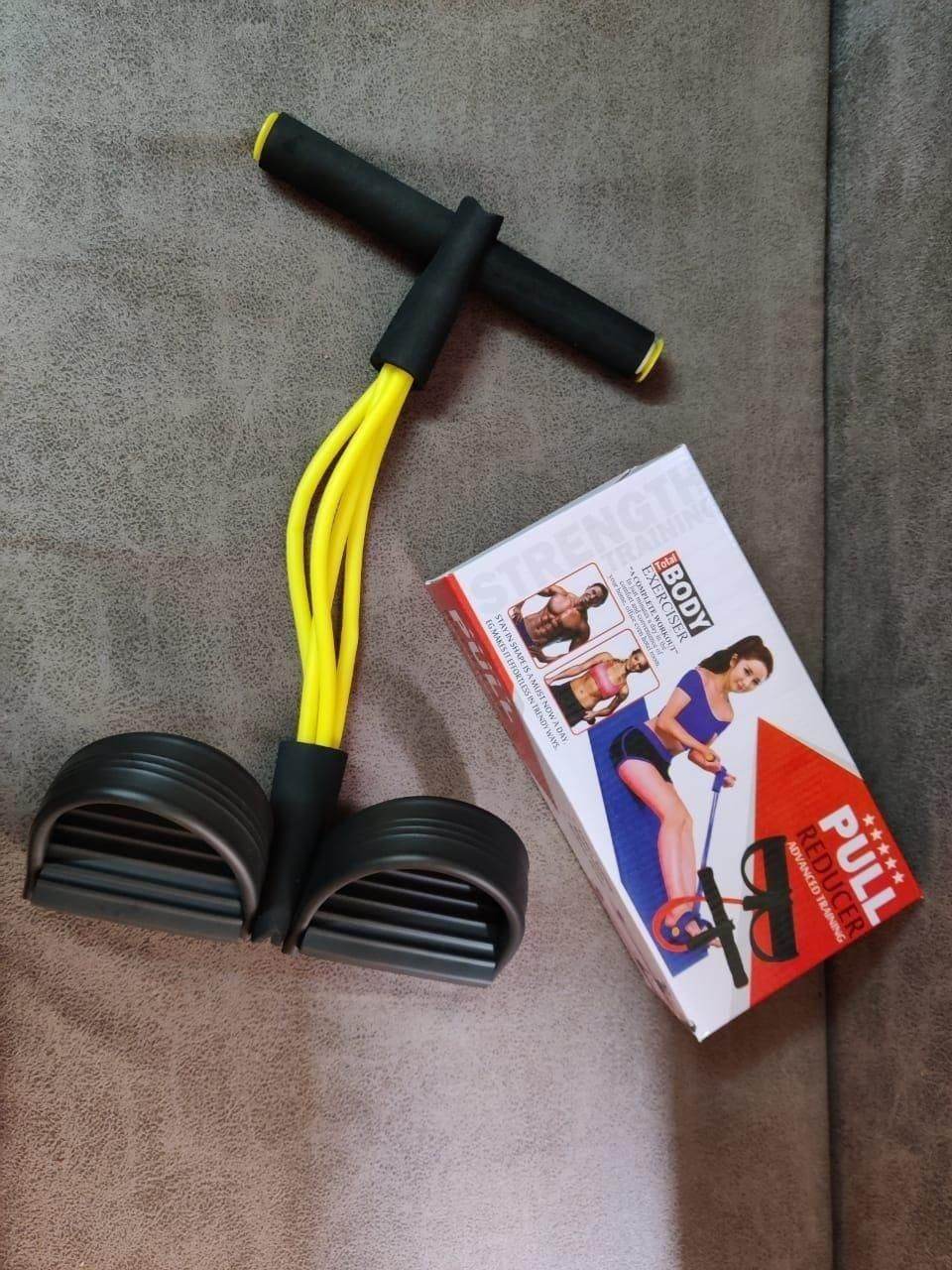 Yellow yoga resistance band for exercise with black handles and foot pedals next to product box