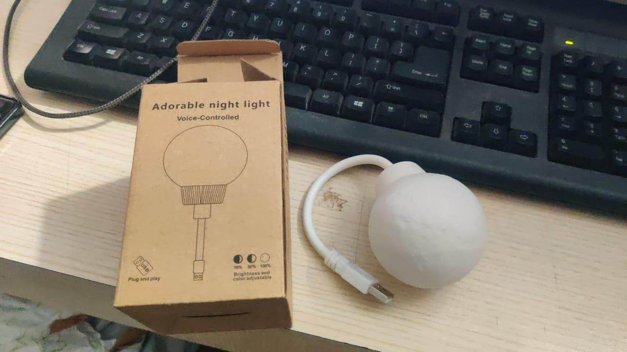 3D moon lamp night light with USB cable next to brown packaging box on desk near keyboard