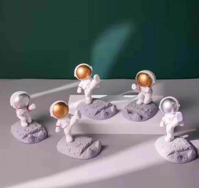 Set of astronaut phone stand models with gold and silver helmets on moon surface base