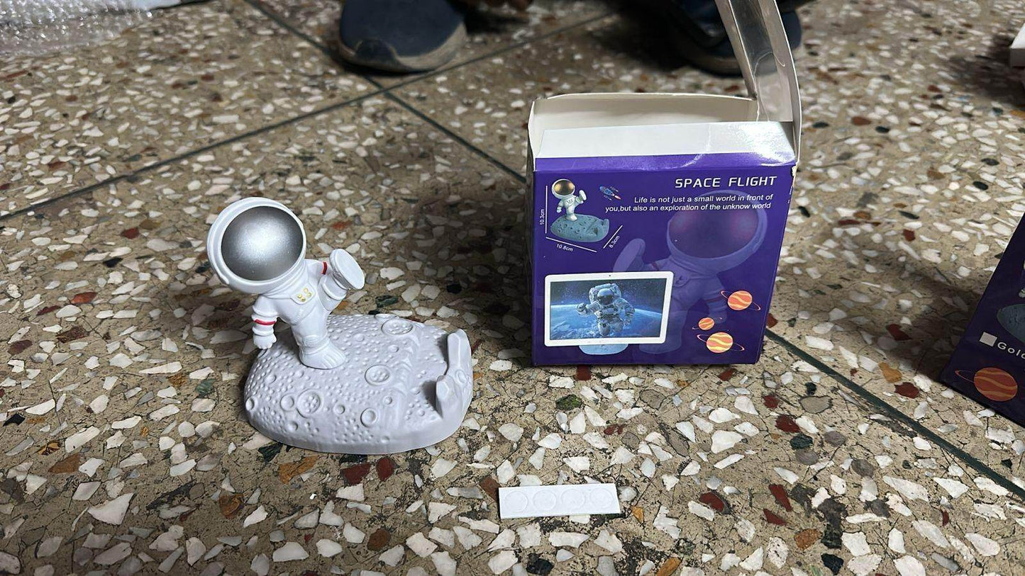 Astronaut phone stand holding a phone on a moon surface base next to its purple space flight packaging