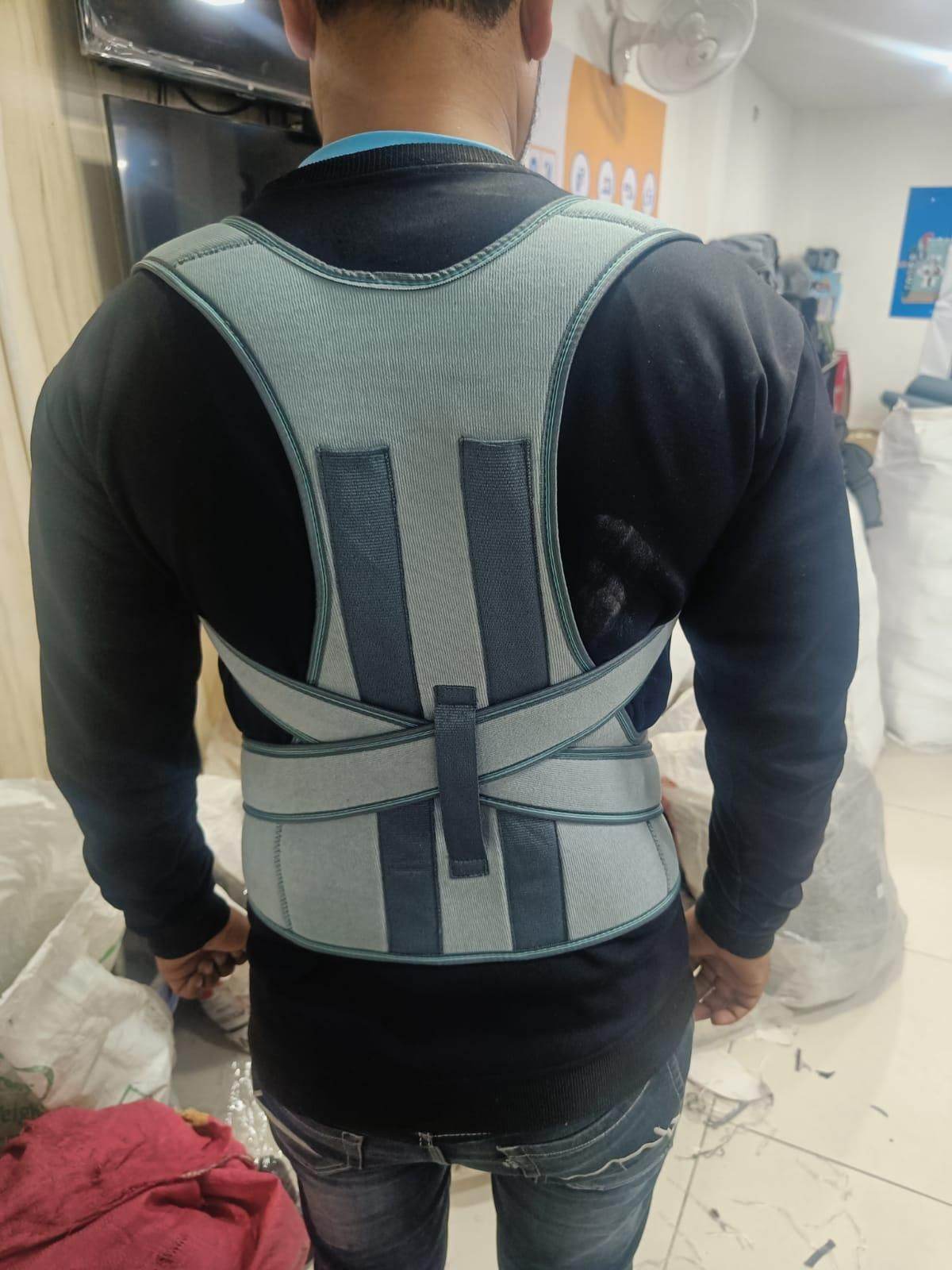 Man wearing a gray and black posture corrector back brace with adjustable straps indoors
