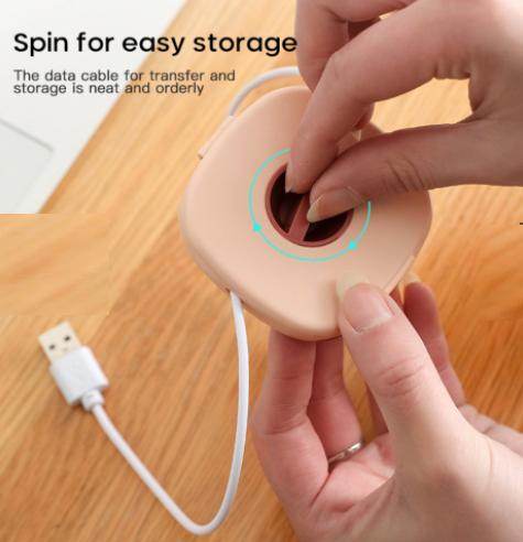 Hands using a compact USB cable holder to neatly store and organize a white USB cable on a wooden surface