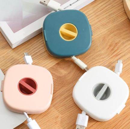 Three compact USB cable holders in blue, pink, and white colors neatly organizing USB cables on a wooden surface