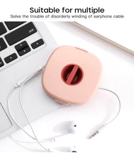 Compact USB cable holder in pink organizing earphone cables next to laptop keyboard