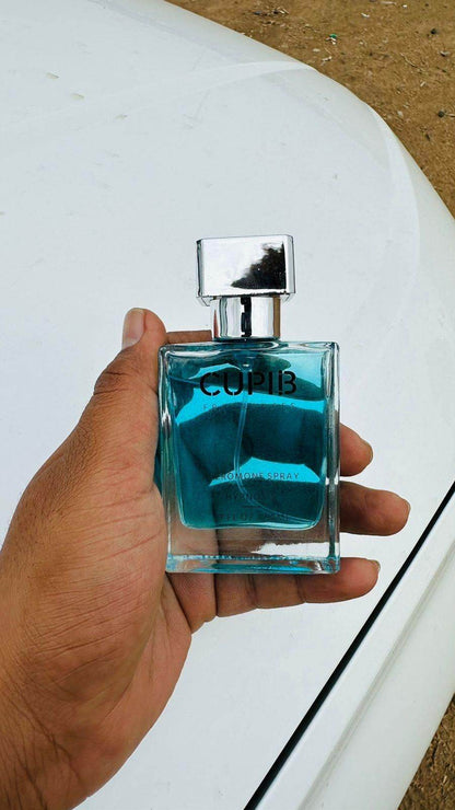 Hand holding a blue glass bottle of pheromone cologne for men with silver cap outdoors