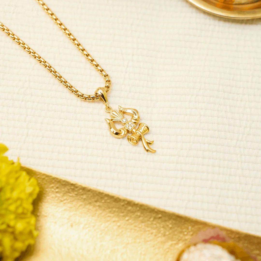 Gold Trishul pendant with chain featuring intricate design and small gemstone centerpiece on textured surface