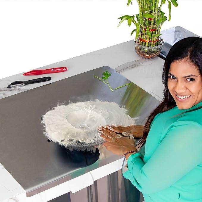 Woman using a stainless steel chopping board with dough and herbs on a kitchen countertop