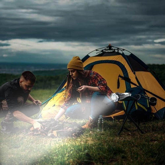 Portable rechargeable LED flashlight illuminating a campsite with two people near a yellow and blue tent at dusk
