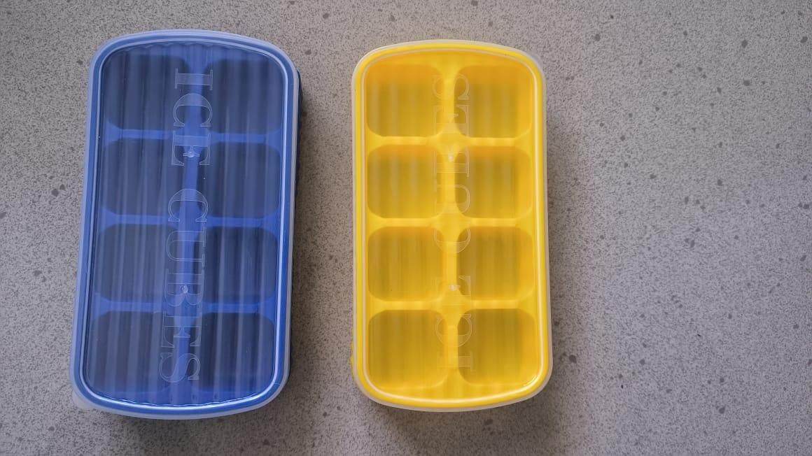 Blue and yellow small ice cube mold for cocktails with multiple compartments on gray surface