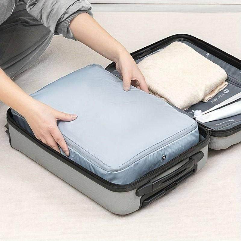 Gray space saving luggage organizer being packed into an open gray suitcase with folded clothes inside