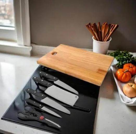 Set of stainless steel knives for home use displayed on a black surface next to a wooden cutting board