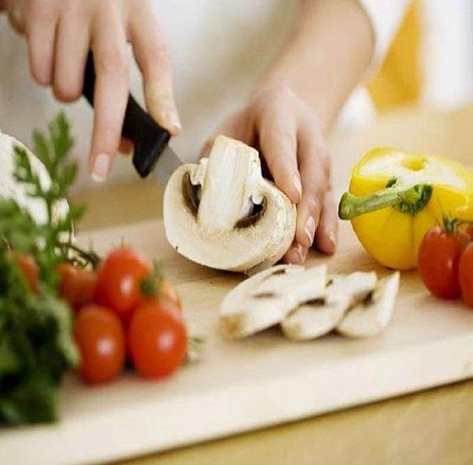 Person slicing mushroom with stainless steel knives for home use on a wooden cutting board with vegetables