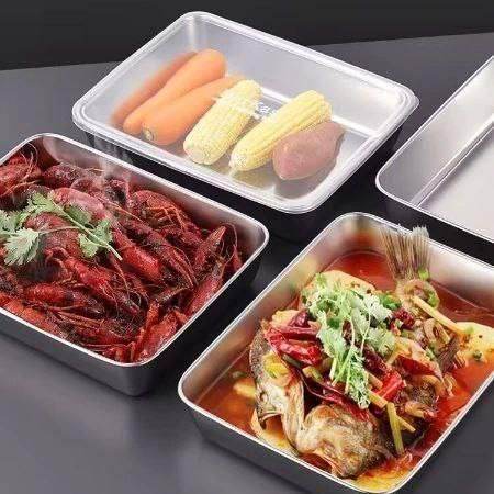Multi-purpose kitchen container with cover holding corn carrots sweet potato alongside stainless steel containers with cooked seafood and fish dishes