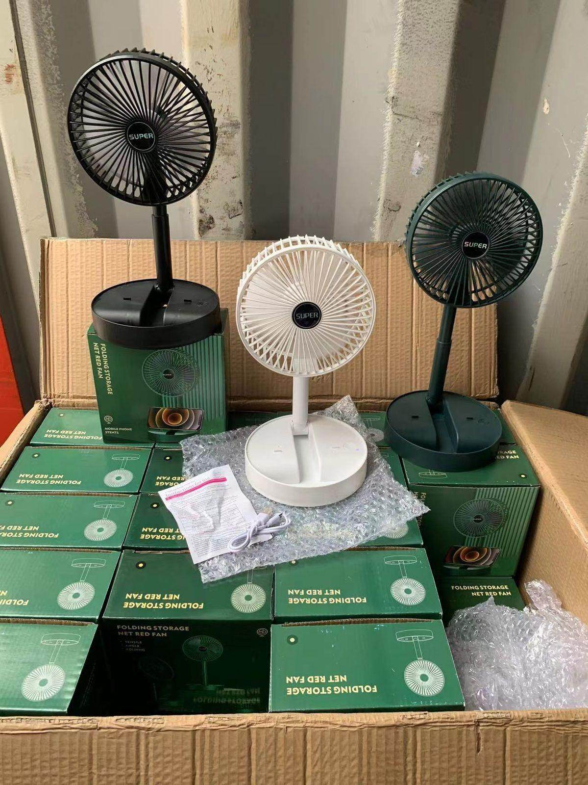Three rechargeable table fans in black, white, and green displayed on packaging boxes inside a cardboard box